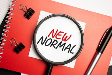 Masaüstünde raporlar, not defterleri, hesap makinesi, nakit para ve NEW NORMAL yazılı sarı çıkartma var. İş konsepti