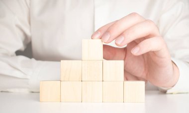 Mavi gömlekli bir iş adamı, boş tahta blokları elleriyle düzenliyor. Beyaz ahşap bir masanın üzerine yerleştirilmiş. İş stratejisi ve eylem planı. Boşluğu kopyala.