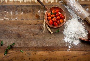 Küçük bakır tencerede kiraz domatesleri, ahşap masa üzerinde merdane ve un yazı için boş alan, üst görünüm, kopyalama alanı.