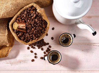 İki tane sade kahve fincanı ve kahve poşeti açık pembe ahşap masa üzerinde kahve çekirdekleri, ev yapımı, çiftlik tarzı, üst görünüm.