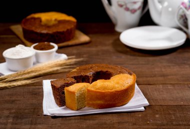 Çikolata ve buğday unlu kek ve ahşap üzerine kumaş dilimlenmiş arkaplanda kek, buğday dalı, beyaz tabak, yanında beyaz çizme.