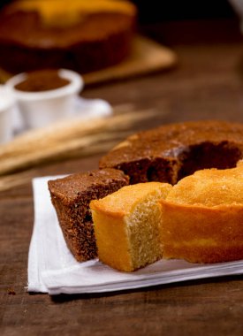Çikolata ve buğday unlu kek ve ahşap üzerine kumaş dilimlenmiş arkaplanda kek, buğday dalı, beyaz tabak, yanında beyaz çizme.