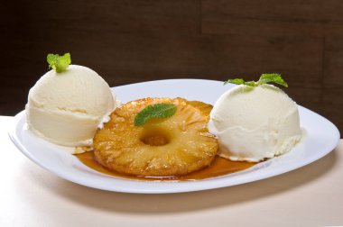 Bir dilim kavrulmuş ananas, iki kepçe vanilyalı dondurma ve beyaz tabakta karamelize edilmiş.