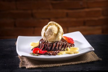 Çikolatalı pasta, dondurma ve arka planda tuğlalar olan bir dilim çilek.