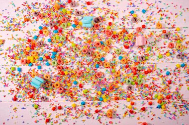 Renkli şeker ve açık pembe arka planda serpiştirilmiş şekerler.