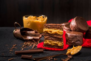 Dulce de leche ile alfajore, tencere ve kaşık dolusu süt kırmızı bez üzerinde tatlı ve çikolata talaşı