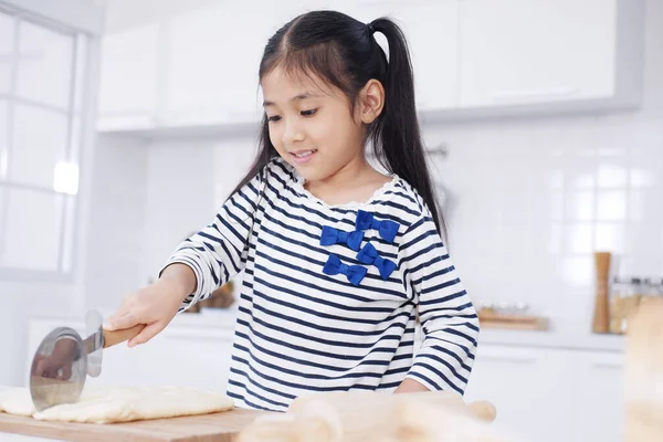 Smiling Asian little asian girl child is learning and enjoying for baking cookies bakery on wooden Cutting board in kitchen. Homemade pastry for bread. Family love and Homeschool.