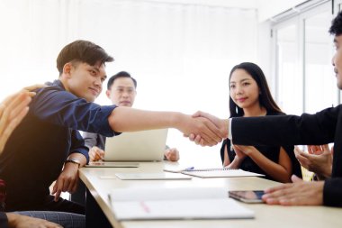 Gülümseyen Asyalı iş adamları ve siyah takım elbiseli takım çalışması, ofisteki toplantı odasında büyük bir proje için ortaklaşa el sıkışıyor. İş ve pazarlama kavramı.