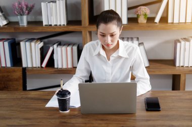 Asian businesswoman is working or online shopping with laptop and drinking hot coffee in workspace at office. Collegian woman are researching information on the Internet in library at the university.