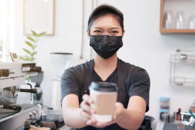 Gülümseyen Asyalı genç barista kadın, kovid19 hastalığını önlemek ve kafede sıcak kahve tutmak için maske takıyor. Kafe ve kafe işine başla. Sağlıklı ve İş Konsepti.