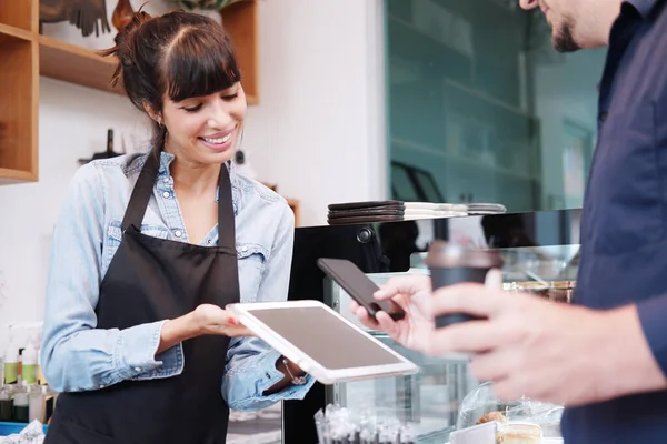 Kafkasyalı genç kadın, kahve dükkanındaki tezgahta ödeme yapmak için akıllı telefon tarama şifresini tablet olarak kullanarak müşteri için tablet tutuyor. Para konsepti olmayan dijital ödeme teknolojisi.