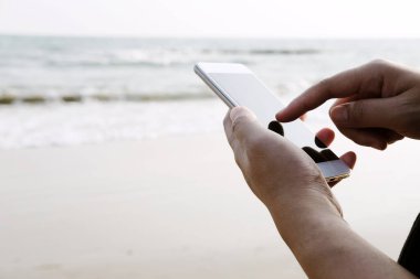 Kapalı el kamerasında akıllı telefon ve internetteki internet ve deniz kenarındaki iş gezileri için ekrana dokunuyor. Tatil konsepti teknolojisiyle tatil ve rahatlama