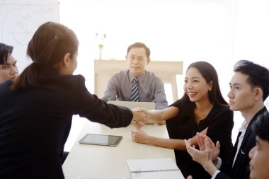 Siyah takım elbiseli başarılı Asyalı iş kadınları, ofiste büyük bir proje için ortaklarıyla tokalaşıyor. İş ve pazarlama kavramı.