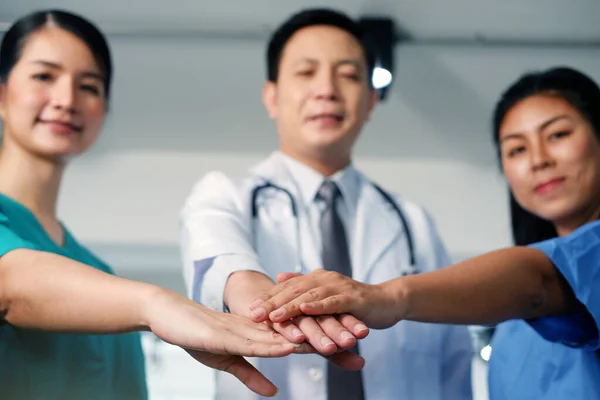 アジアの主任医師男が外科医の女性と手をつないでいる一緒に青と緑の外科用ガウンを着ている 病院の会議室で笑顔の医療チーム 集中して手を閉じて — ストック写真