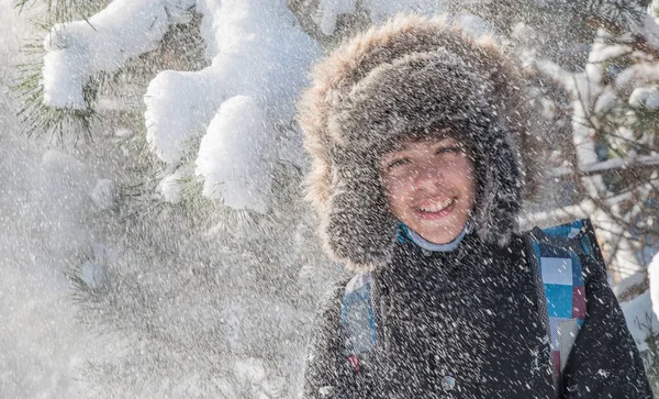 Kar taneleri düşen ve güneşte parlayan kar kürklü bir şapkayla kış ormanında bir genç..