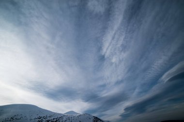 Karanlık bir kış gökyüzünün altında karlı kış dağları.