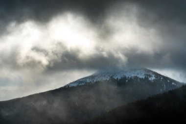Karanlık bir kış gökyüzünün altında karlı kış dağları.