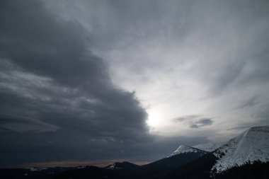 Karanlık bir kış gökyüzünün altında karlı kış dağları.