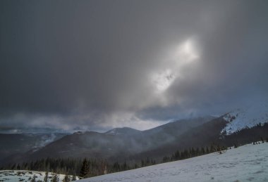 Karanlık bir kış gökyüzünün altında karlı kış dağları.