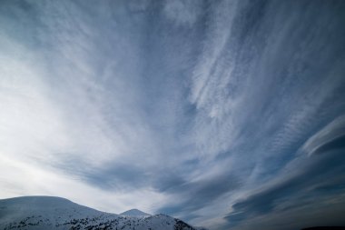 Karanlık bir kış gökyüzünün altında karlı kış dağları.