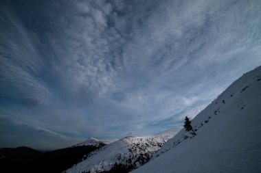 Karanlık bir kış gökyüzünün altında karlı kış dağları.
