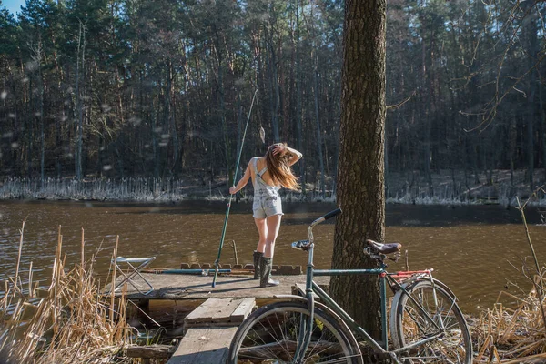 夕暮れ時の暖かい夏の日に湖のそばでデニムのショートパンツと古い自転車の女の子 — ストック写真