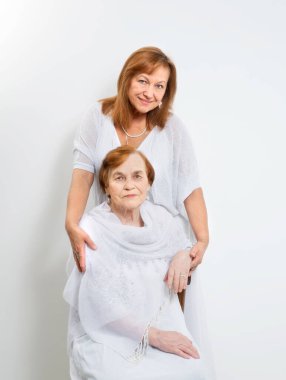 Kıdemli anne - bir emekli ve beyaz arka planda açık renk elbiseli yetişkin kızı..