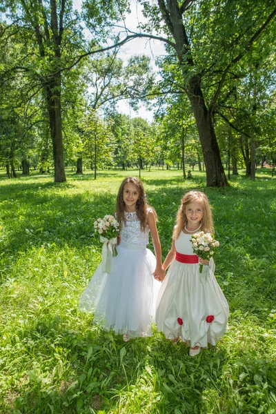 Parkta beyaz elbiseli iki küçük kız kardeş yaz yeşilliklerinin arasında güneşin altında.