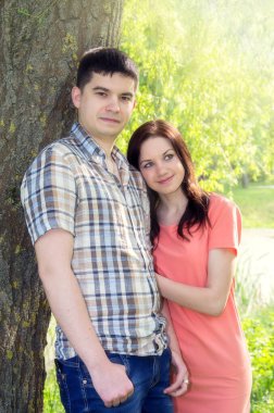 Pembe elbiseli bir kız ve genç bir adam bir ağacın yanında duruyorlar. Yumuşak odaklanma. Bulanık arkaplan.