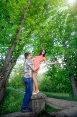 Parktaki taş basamaklarda oturan genç çift. Yaz yeşilliğinin arka planında kadın ve erkek.