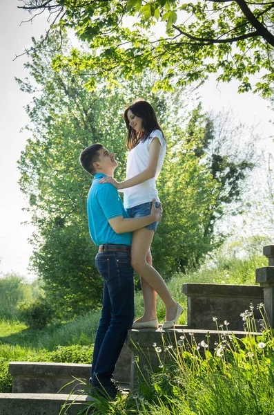 Parktaki taş basamaklarda oturan genç çift. Yaz yeşilliğinin arka planında kadın ve erkek.