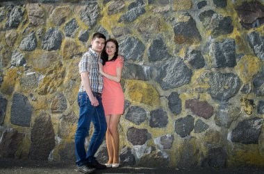 Yosun ve yosunla kaplanmış eski bir taş duvarın yanında birbirine aşık bir çift. Kırmızı elbiseli genç bir kız ve kot pantolonlu genç bir adam..