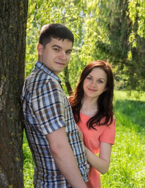 Pembe elbiseli bir kız ve genç bir adam bir ağacın yanında duruyorlar. Yumuşak odaklanma. Bulanık arkaplan.