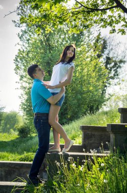 Parktaki taş basamaklarda oturan genç çift. Yaz yeşilliğinin arka planında kadın ve erkek.