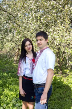 Bahar bahçesinde çiçek açan bir ağacın yanında, beyaz işlemeli gömlekli genç bir çift..