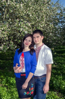 Bahar bahçesinde çiçek açan bir ağacın yanında işlenmiş gömlekli genç bir çift..