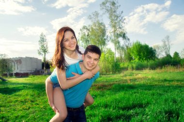 Genç bir adam, güzel gülümseyen kadınını parkta sırtında taşır. Birbirine aşık çiftler birlikte eğleniyor..