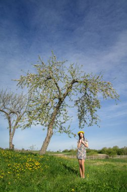 Girl with a wreath of dandelions near an old flowering tree.