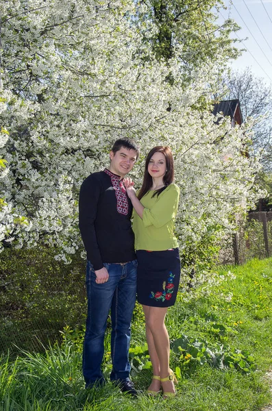 Bahar bahçesinde çiçek açan bir ağacın yanında işlenmiş gömlekli genç bir çift..