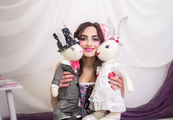 一个聪明的 黑头发的女孩 看起来像一个玩具娃娃与兔子娃娃玩耍 紫罗兰色调 白色背景 — 图库照片