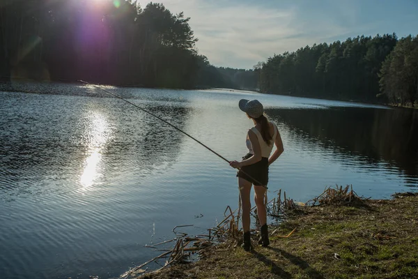 森の湖のほとりに立って釣竿で魚を捕る少女. — ストック写真