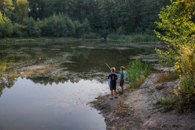 İki çocuk eski bir orman gölünde oltayla balık tutuyor..