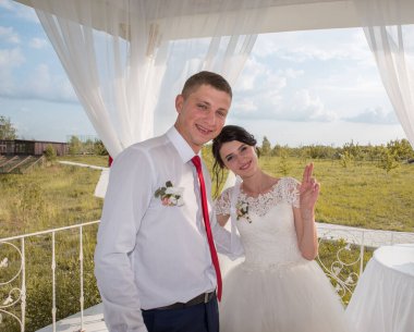 Gelin ve damat açık havada güneşli bir yaz gününde beyaz bir gölgelik altında.