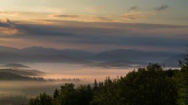 Bulutlar hareket eder ve gün doğumunda dağ zirveleri arasında yayılır..