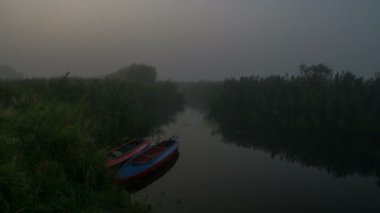 Dawn with fog on the river. Sunrise over bright kayaks that stand on the wat
