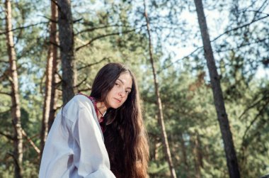 Uzun saçlı Ukraynalı kız ormanda işlenmiş ulusal bir gömlek giyiyor.