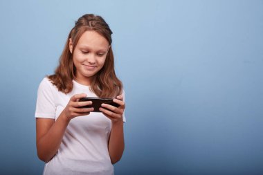 Mavi arka planda akıllı telefonu olan genç bir kız.