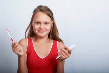 11 yaşında neşeli, güzel bir kız beyaz bir arka planda dişlerini fırçalıyor.