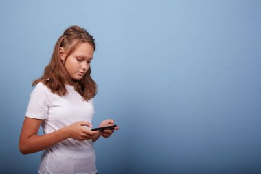 Mavi arka planda akıllı telefonu olan genç bir kız.