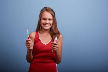 11 yaşında neşeli, güzel bir kız dişlerini mavi bir arka planda fırçalıyor.